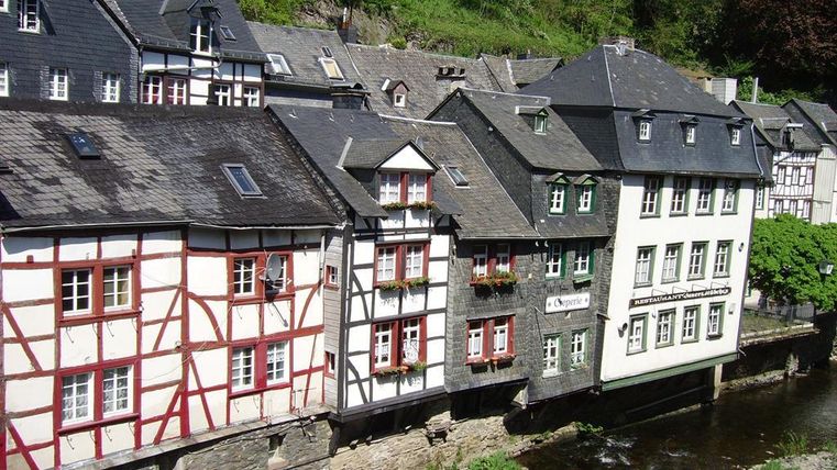Eine malerische Reihe von Häusern am Fluss mit Fachwerkarchitektur. Umgeben von grüner Natur und einem klaren Himmel.