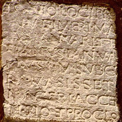 Eine alte Steininschrift mit eingravierten Buchstaben. Die Zeichen sind teilweise verwittert und unleserlich.