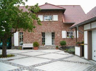 Ein hübsches zweigeschossiges Haus aus roten Ziegeln. Vor dem Haus gibt es einen gepflasterten Eingangsbereich mit einer Sitzbank und Bäumen.