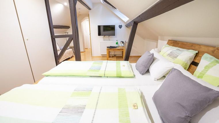 Ein gemütliches Schlafzimmer mit zwei Betten, die mit hellen, gestreiften Bettwäsche dekoriert sind. Die Holzdecke und der Fernseher im Hintergrund sorgen für ein einladendes Ambiente.