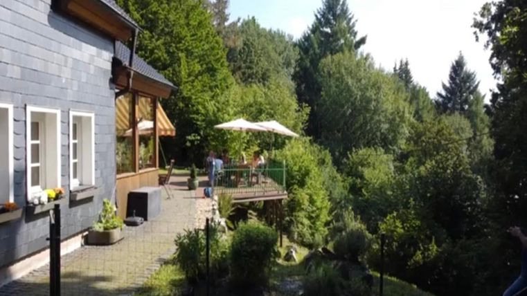 Ein gemütliches Haus umgeben von Bäumen und Grünflächen. Auf der Terrasse stehen Sonnenschirme und es gibt einen schönen Ausblick ins Grüne.