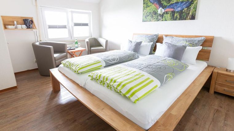 Ein modernes Schlafzimmer mit einem großen Doppelbett und bunten Kissen. In der Ecke stehen zwei gemütliche Sessel und ein Tisch.