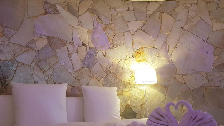 Ein gemütliches Schlafzimmer mit einem großen Bett und weichen Kissen. Die abgerundete Steinwand und die sanfte Beleuchtung schaffen eine entspannende Atmosphäre.