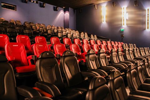 Ein modernes Kino mit vielen leeren Sitzen in Schwarz und Rot. Die bequemen Sessel sind aufsteigend angeordnet und bieten eine angenehme Atmosphäre.