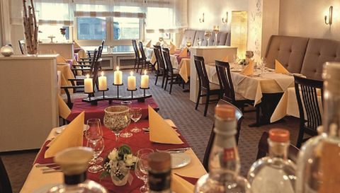 Ein elegantes Restaurant mit gemütlicher Atmosphäre. Tische sind mit roten und gelben Tischdecken sowie Kerzen dekoriert.