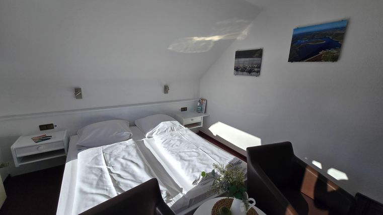 Ein gemütliches Zimmer mit zwei Betten und modernem Design. Es gibt einen kleinen Tisch mit einer Blumenvase und bequeme Stühle.