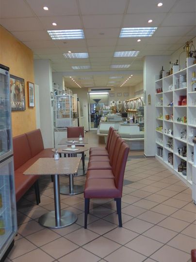 Ein gemütliches Café mit roten Sitzbänken und hellen Wänden. Im Hintergrund sind Regale mit verschiedenen Produkten zu sehen.