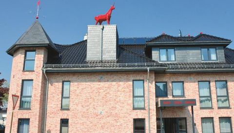 Ein modernes Gebäude mit roten Ziegeln und großen Fenstern. Auf dem Dach steht eine auffällige rote Skulptur eines Tieres.