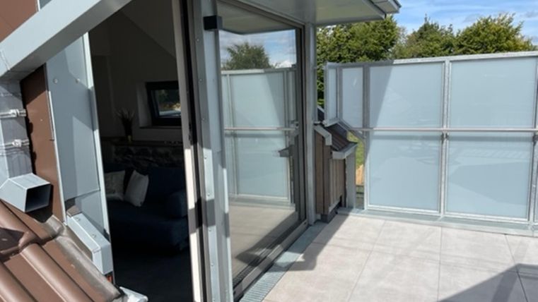 Ein moderner Balkon mit Glasgeländer und einer schönen Aussicht. Die offenen Türen führen ins Innere des Raumes.