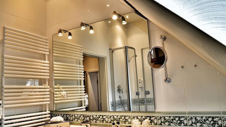 Ein modernes Badezimmer mit einem Waschbecken und einem großen Spiegel. Die Wände sind hell gefliest, und es gibt eine Dusche sowie Handtuchhalter.
