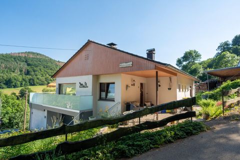 Ein modernes Haus in einer ländlichen Umgebung mit einer Glasveranda. Im Hintergrund sind grüne Hügel und Bäume zu sehen.