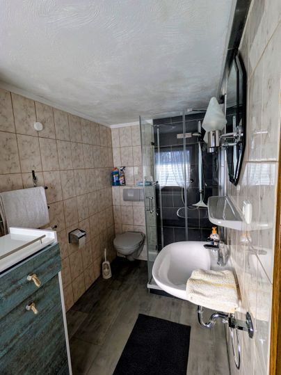 Ein modernes Badezimmer mit Dusche, Waschbecken und Badewanne. Die Wände sind gefliest, und es gibt eine graue Matte auf dem Boden.