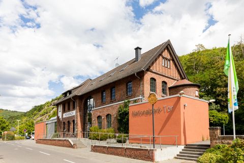 Ein historisches Gebäude mit rotem Ziegelmauerwerk und einem modernen Anbau. Die Umgebung ist grün und einladend, ideal für Besucher.