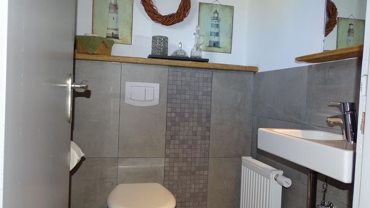 Ein modernes Badezimmer mit einer weißen Toilette und einem kleinen Waschbecken. An der Wand hängen dekorative Bilder von Leuchttürmen und ein Kranz.