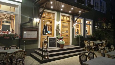 Ein einladendes Restaurant mit Holzverkleidung und beleuchteten Fenstern. Vor dem Eingang stehen Tische und Stühle für Gäste im Freien.