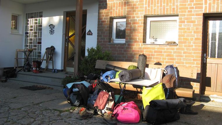 Eine Ansammlung von Rucksäcken und Gepäck liegt vor einem Eingang. Der Platz ist hell beleuchtet und bietet einen einladenden Eindruck.