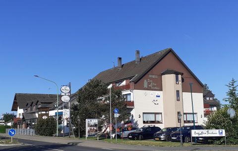 Ein gemütliches Hotelgebäude mit einer Mischung aus modernen und traditionellen Elementen. Vor dem Hotel stehen mehrere Autos und im Hintergrund sind weitere Gebäude zu sehen.