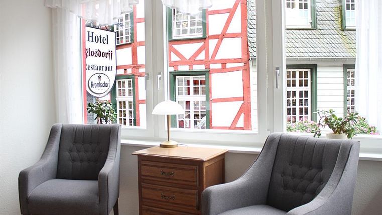 Ein gemütlicher Raum mit zwei grauen Sesseln und einem Holztisch. Durch das Fenster ist ein schöner Ausblick auf ein Gebäude mit orangefarbenen Fachwerk zu sehen.