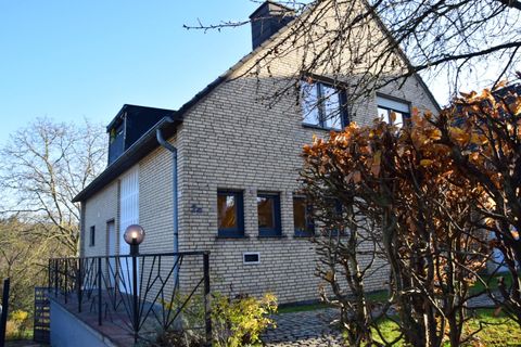 Ein charmantes Haus mit einer Backsteinfassade und großen Fenstern. Der Garten ist mit Bäumen und Sträuchern gestaltet.