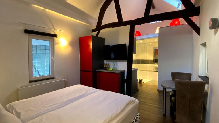 Ein gemütliches Zimmer mit einem Doppelbett und Holzdeckenbalken. Die Ausstattung umfasst einen Kühlschrank und einen Esstisch.