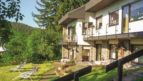Ein schönes Haus mit großflächigen Fenstern und einem Balkon inmitten von Grünflächen. Im Vordergrund stehen Liegen und Blumenbeete.