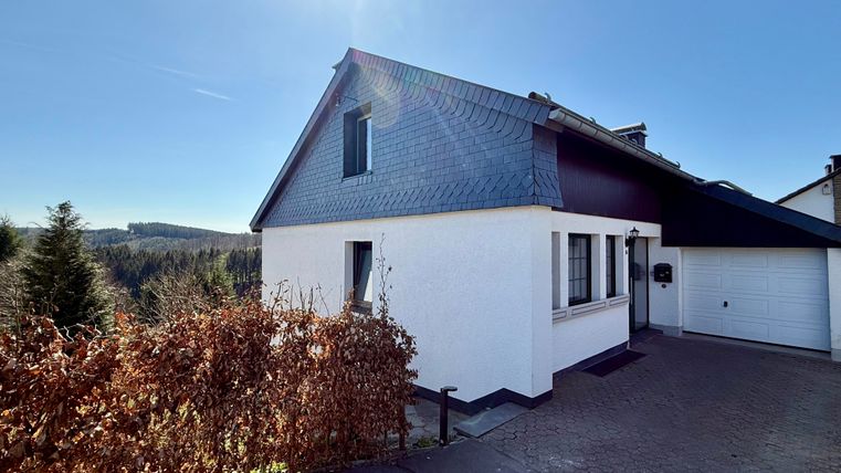 Ein modernes Haus mit einem blauem Dach und einer weißen Fassade. Im Hintergrund sind Bäume und ein klarer Himmel zu sehen.