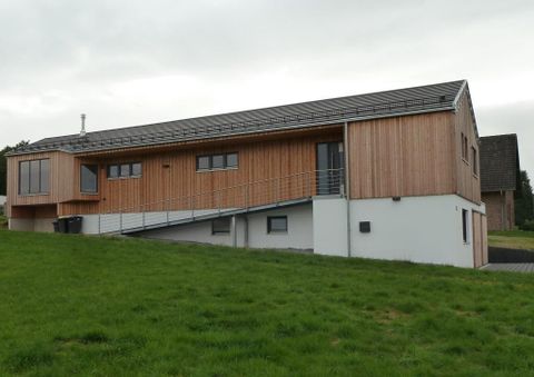 Ein modernes, zweigeschossiges Haus mit Holzverkleidung. Es steht auf einer Wiese und hat große Fenster.