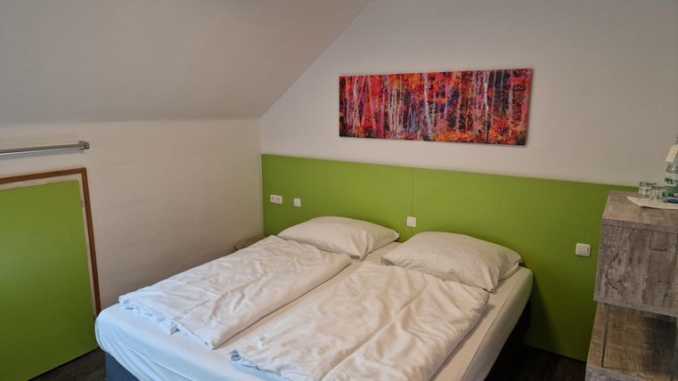 Ein gemütliches Schlafzimmer mit einem Doppelbett und einer modernen grünen Wand. An der Wand hängt ein buntes Kunstwerk, das den Raum dekoriert.