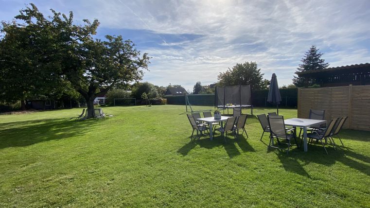 Ein schöner Garten mit grünem Rasen und einem großen Baum. Es stehen mehrere Tische und Stühle in der Mitte des Gartens.
