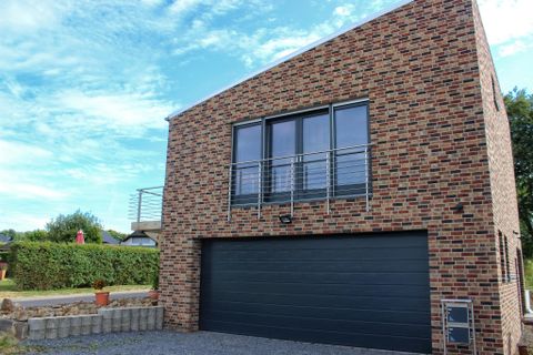 Ein modernes, zweigeschossiges Haus aus Backstein mit großen Fenstern. Vor dem Gebäude befindet sich eine Garage und der Himmel ist klar und blau.