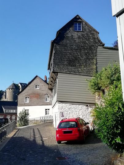 Eine alte Straße mit historischen Gebäuden und einem roten Auto. Im Hintergrund sind weitere Gebäude und eine Zitadelle zu sehen.