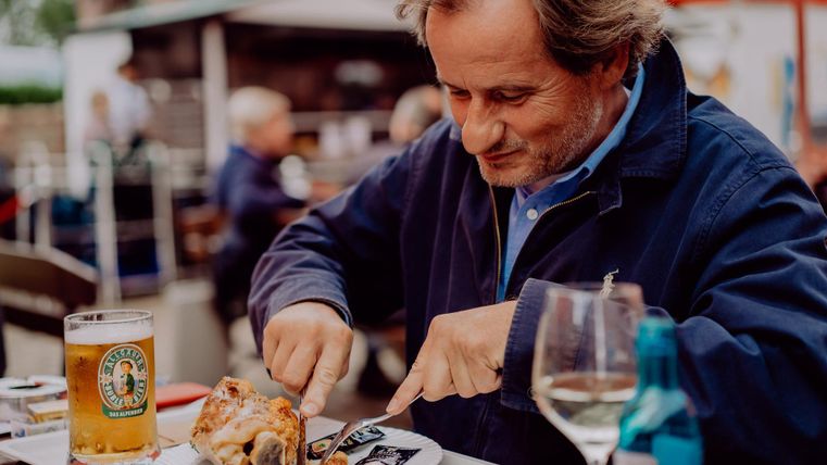 Ein Mann sitzt an einem Tisch und genießt sein Essen. Vor ihm stehen ein Bier und ein Glas Wein.