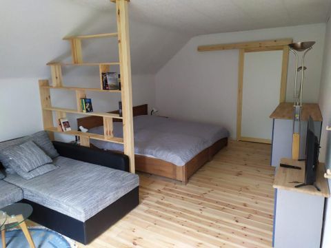 Ein modernes Zimmer mit einem Doppelbett und einer Sitzecke. Die Holzregale und der elegante Holzboden schaffen eine gemütliche Atmosphäre.