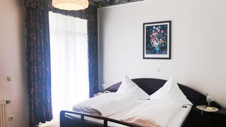 Ein gemütliches Schlafzimmer mit einem Doppelbett und zwei Kissen. Große Fenster lassen viel Tageslicht herein und der Raum ist geschmackvoll dekoriert.
