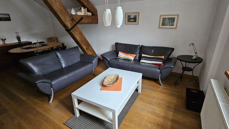 Ein gemütliches Wohnzimmer mit zwei grauen Sofas und einem niedrigen weißen Tisch. An der Wand hängen Bilder, und es gibt einen Holzfußboden sowie einige dekorative Elemente.