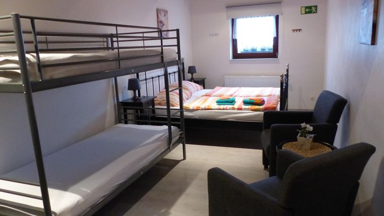 Ein Zimmer mit einem Etagenbett und einem Doppelbett. Es gibt auch einen Sessel und einen kleinen Tisch.