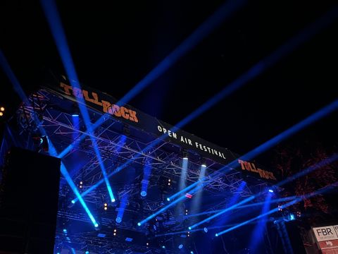 Eine Bühne bei einem Open-Air-Festival mit bunten Lichtern. Der Himmel ist dunkel, und die Atmosphäre ist festlich.