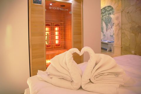 Ein entspannendes Wellnesszimmer mit zwei handtuchförmigen Schwänen, die ein Herz bilden. Im Hintergrund steht eine Infrarotsauna mit warmem Licht.