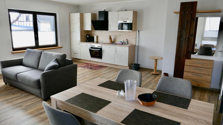 Eine moderne Wohnung mit einer offenen Küche und einem gemütlichen Wohnbereich. Der Tisch ist mit Geschirr gedeckt und es gibt viel Tageslicht durch die Fenster.