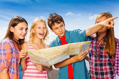 Eine Gruppe von vier Jugendlichen schaut auf eine Landkarte und lacht. Einer von ihnen zeigt auf einen Punkt auf der Karte.