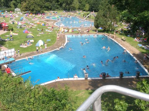 Ein großer Swimmingpool mit vielen Schwimmern und Freizeitaktivitäten. Rundherum sind Liegewiesen und Sonnenschirme aufgestellt.