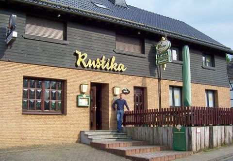 Ein rustikales Restaurant mit der Aufschrift "Rustika" an der Fassade. Vor dem Eingangsbereich steht eine Person auf den Stufen.