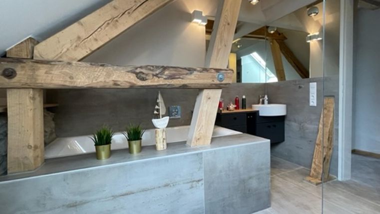 Ein modernes Badezimmer mit einer freistehenden Badewanne und Holzdetails. Die Wände sind in neutralen Farben gehalten und es gibt viel Tageslicht.