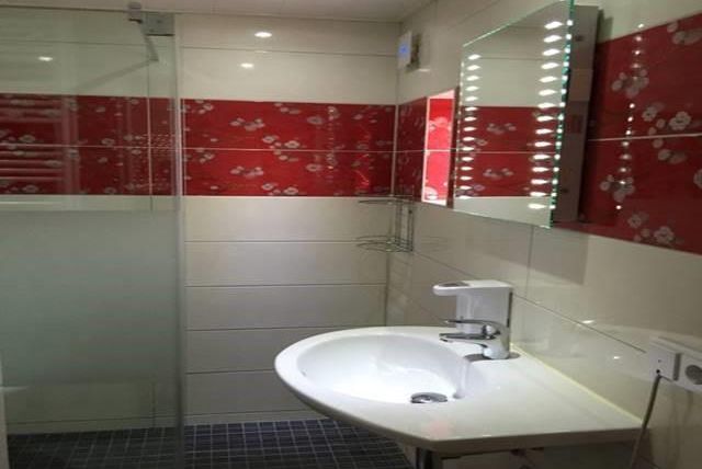 Ein modernes Badezimmer mit einer Walk-in-Dusche und einer eleganten Waschbeckenanlage. Die Wände sind mit weißen Fliesen und roten Akzenten dekoriert.