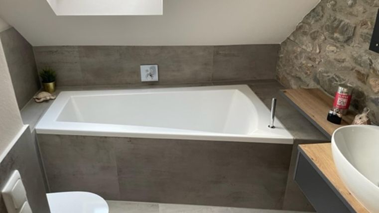 Ein modernes Badezimmer mit einer weißen Badewanne und einem Waschbecken. Die Wände sind teilweise mit Steinverkleidung dekoriert.
