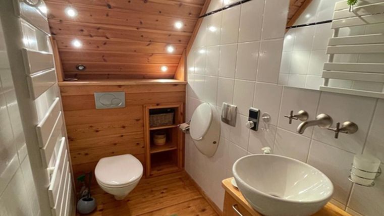 Ein modernes Badezimmer mit Holzwänden und Decken. Es verfügt über eine Toilette, ein Waschbecken und warmes Licht.