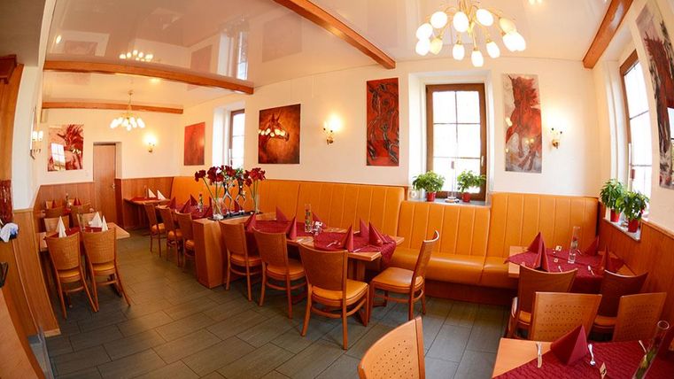 Ein gemütliches Restaurant mit Holzdekor und rötlichen Akzenten. Die Tische sind schön gedeckt und die Wände sind mit Kunstwerken geschmückt.