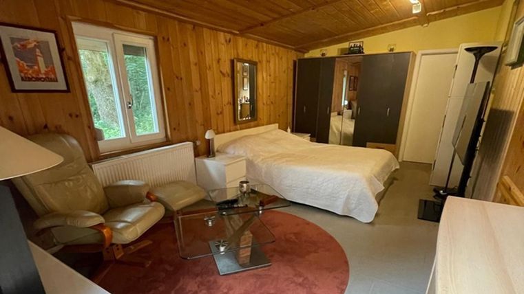 Ein gemütlicher Raum mit Holzwänden und einem Bett. Es gibt eine Sitzecke mit einem Sessel und einem Tisch.