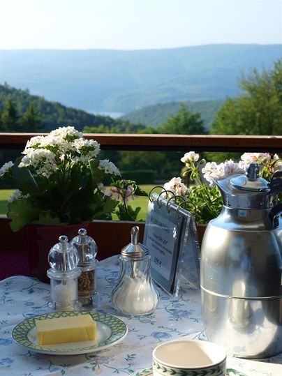 Ein schöner Tisch auf einem Balkon mit Blick auf eine grüne Landschaft. Es gibt Blumen, Butter und Kaffeetassen.