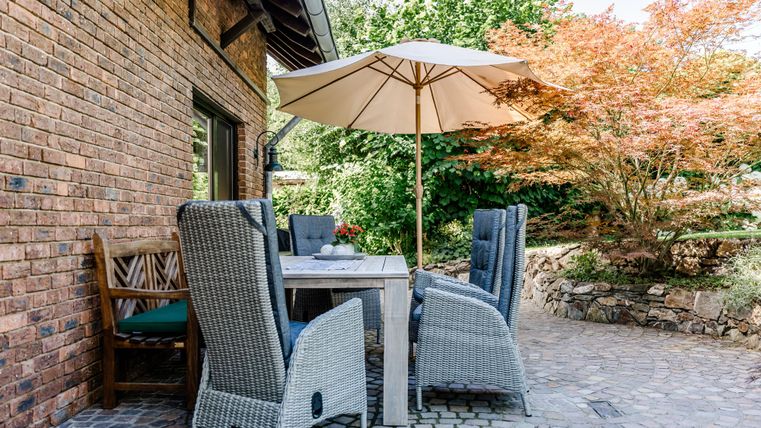 Ein gemütlicher Sitzbereich mit einem Tisch und Stühlen unter einem Sonnenschirm. Der Garten ist grün und gepflegt.